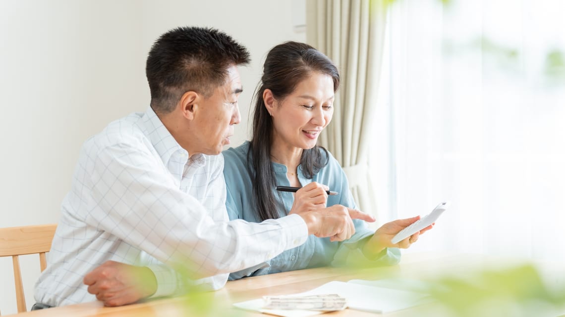 電卓と家計簿で、1か月の費用を確かめるご夫婦のイメージ