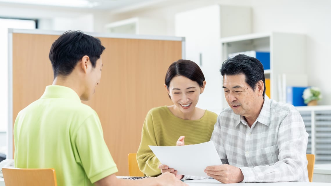 職員から説明を受ける高齢の男性とご家族のイメージ