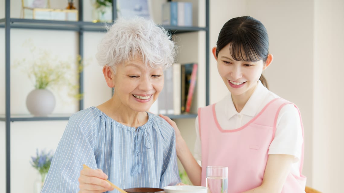 食事をする高齢の女性に、職員がそばで寄り添っているイメージ