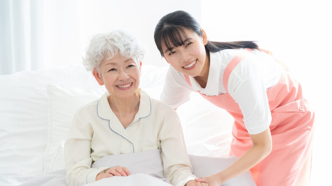 ベッドで過ごす高齢の女性に、職員が寄り添って話しかけるイメージ