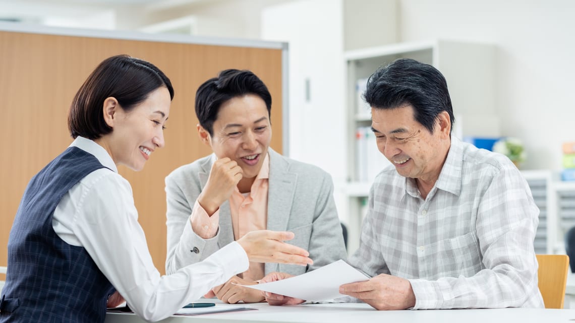 職員から書類を見ながら説明を受ける父と息子のイメージ