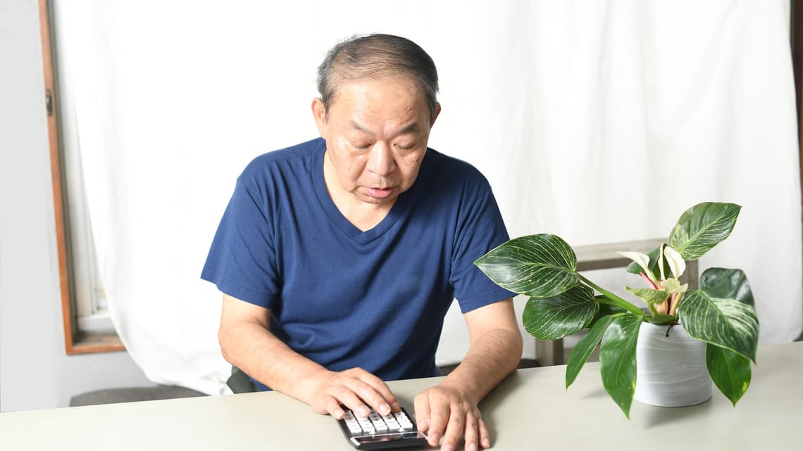 電卓を使って、1か月の費用を確かめる高齢の男性のイメージ