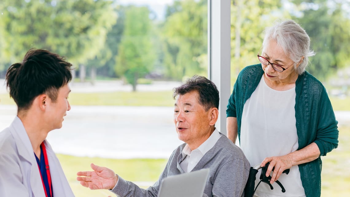 車いすのお父様とお母様に、医師が説明しているイメージ