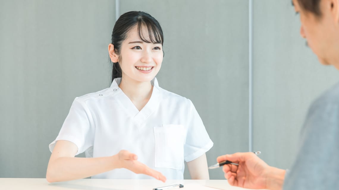 病院の窓口で、看護師が笑顔で説明しているイメージ