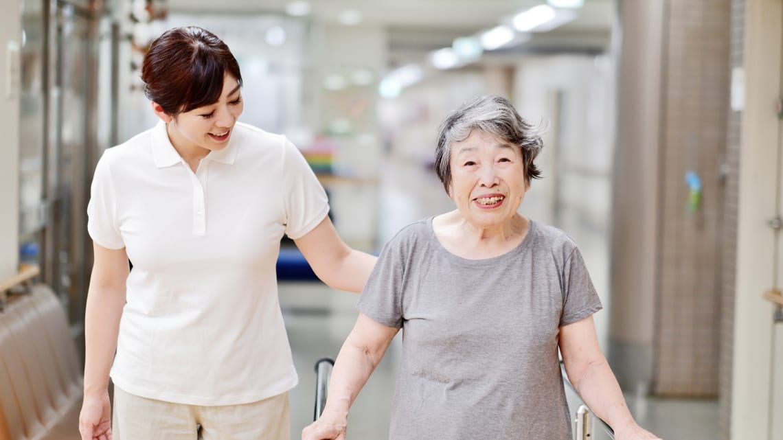 平行棒につかまって歩く練習をするお母様と、付き添う職員のイメージ