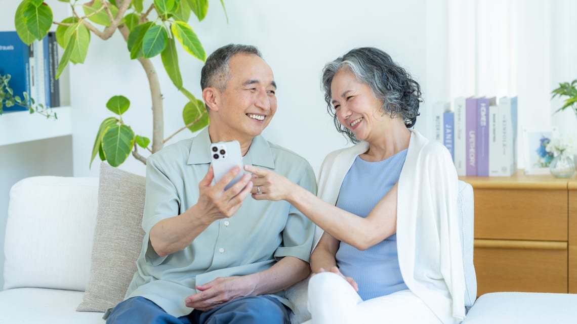 明るいリビングで、並んで笑顔を見せる高齢のご夫婦のイメージ