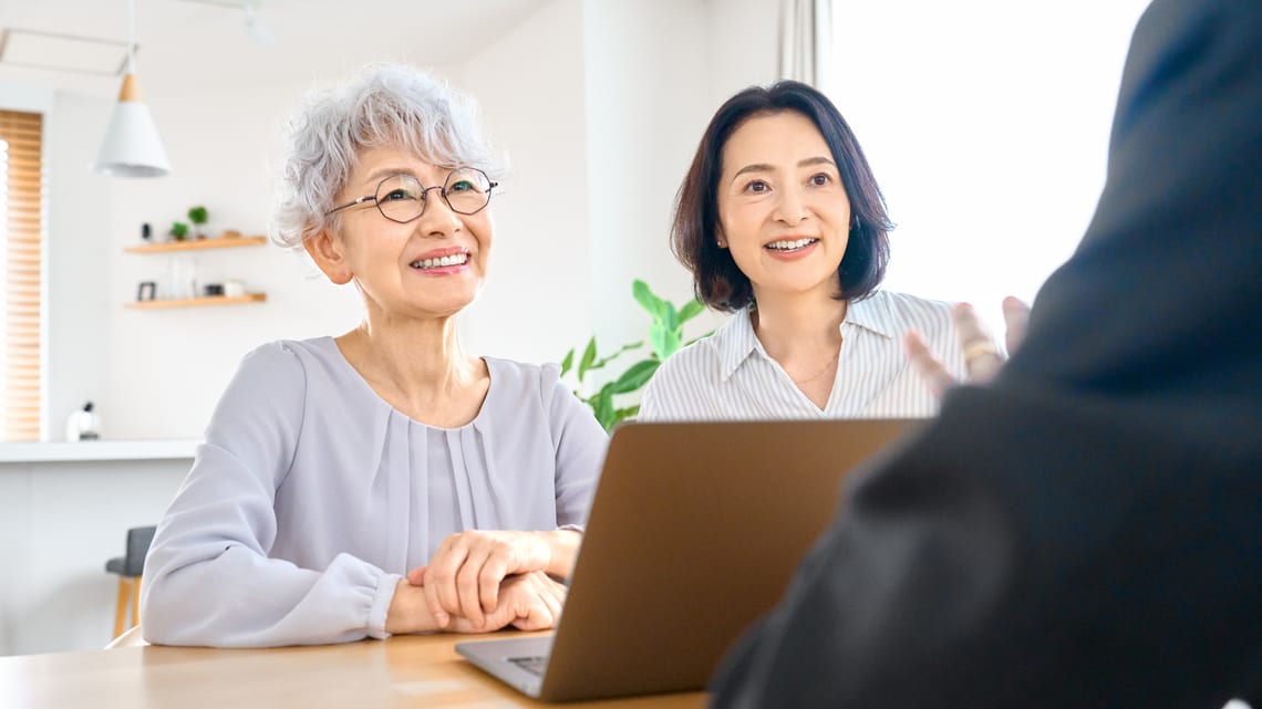 高齢のお母様と娘さんが、相談員と一緒に費用の話をしているイメージ