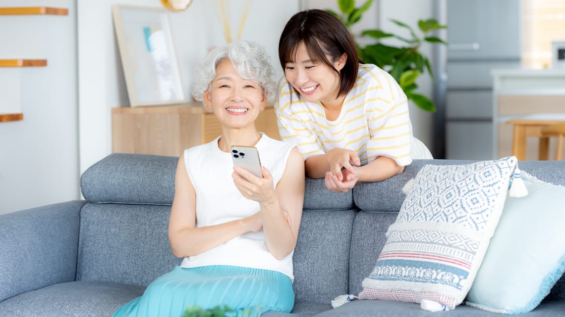 ソファでスマートフォンを見ながら話すお母様と娘さんのイメージ