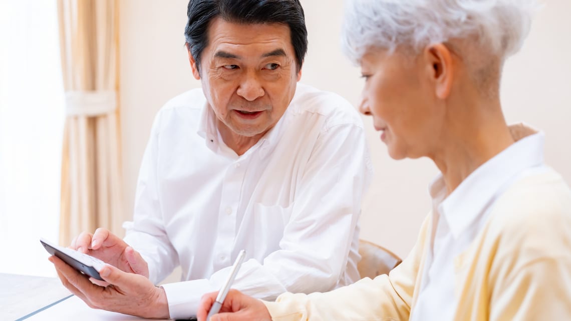 電卓を手に、1か月の費用を確かめる高齢のご夫婦のイメージ