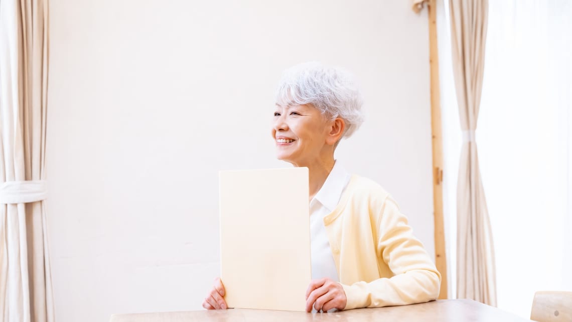 書類のファイルを手に、ほほえむ高齢の女性のイメージ