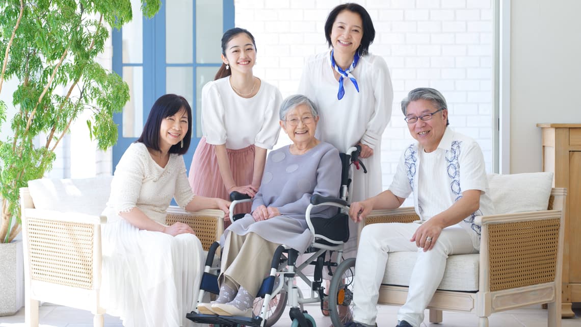 車いすの高齢の女性を囲んで、リビングに集まる家族のイメージ