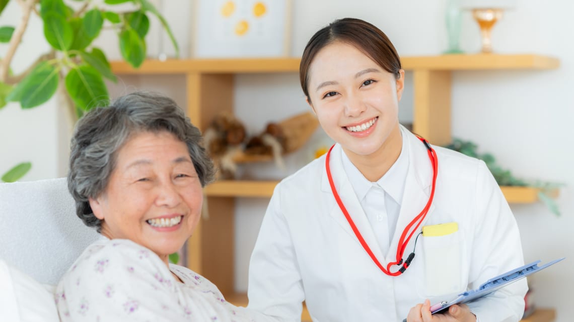 病室のベッドで、看護師と笑顔で話す入院中の高齢の女性のイメージ