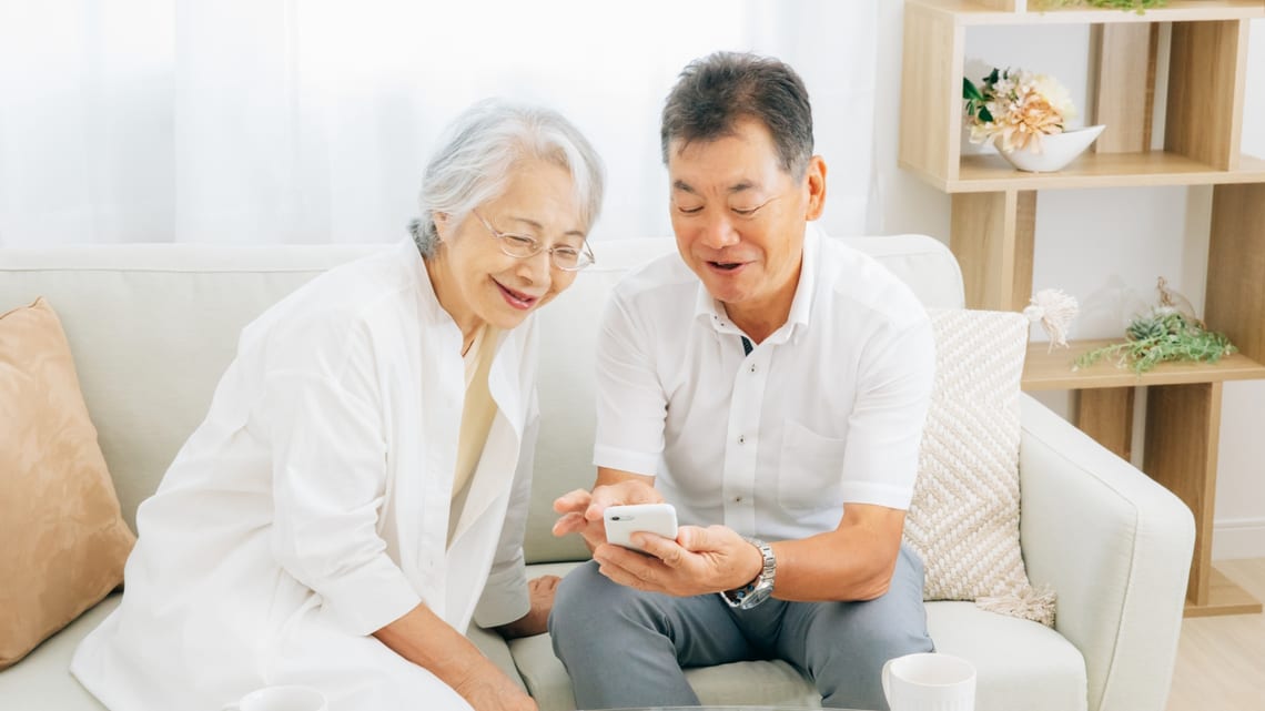 スマートフォンの画面を一緒に見て笑う高齢のご夫婦のイメージ