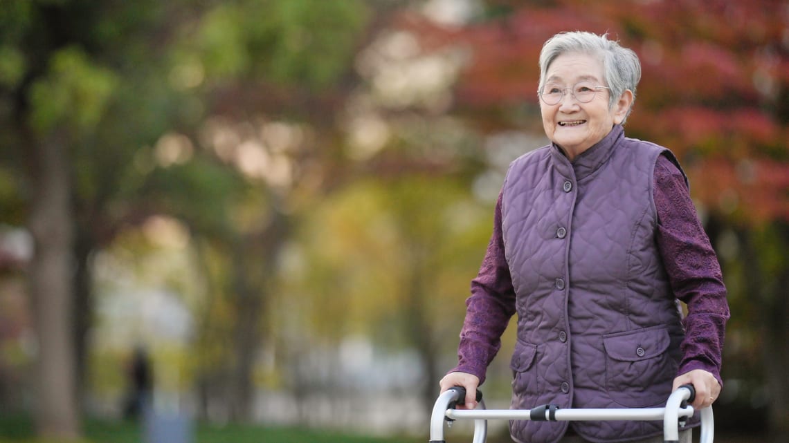 歩行器を使って、笑顔で散歩する高齢の女性のイメージ