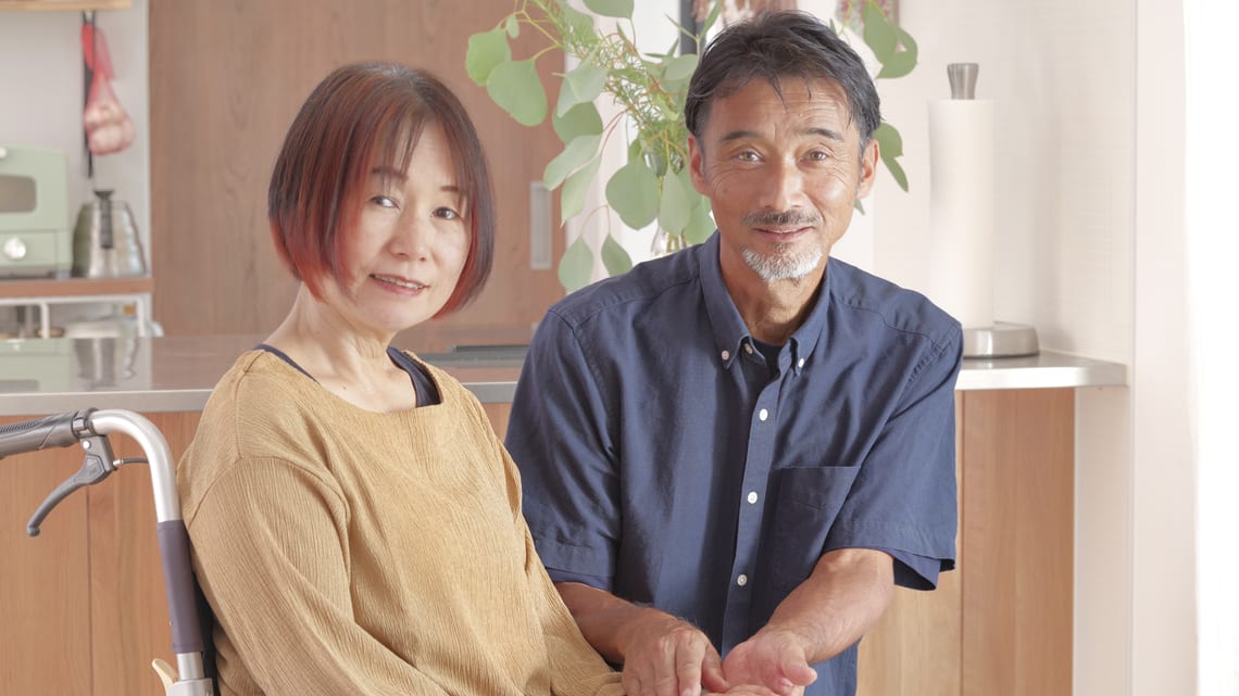 車いすに座る妻に寄り添う夫のイメージ