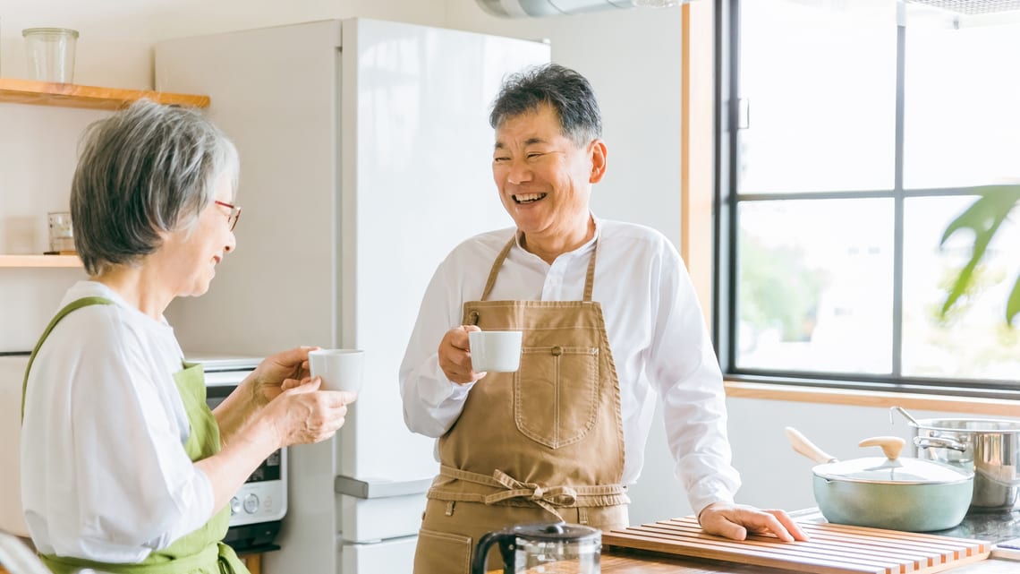 キッチンで、コーヒーを手に笑顔で話す高齢のご夫婦のイメージ